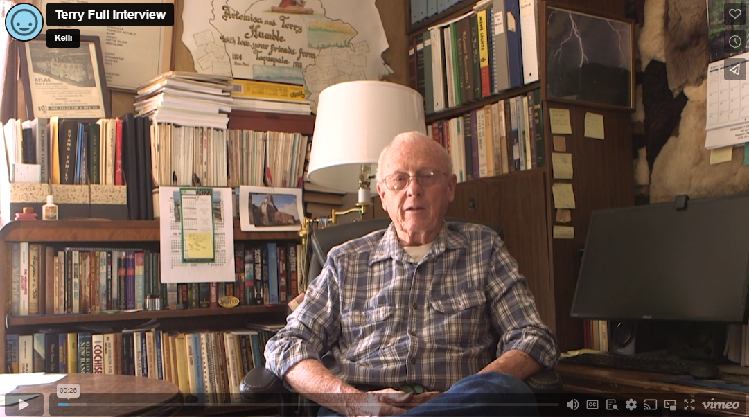 Terry, an elderly man with a blue plaid shirt, sits in his home library