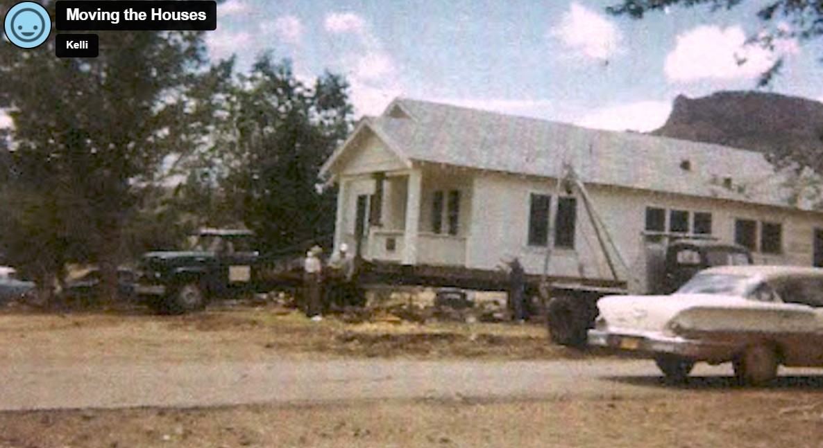 Screenshot at 12:29. Image shows a photo of white house on a trailer being pulled by a truck. There is a 1960s car in the foreground of the image