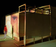 Image of large face from live video footage looking down at a visitor leaving the CompuObscura. Taken by Cal Poly Architecture class students using class-created model and slide projector, Spring 2004.