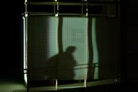Image of grey film frame cast against the side of the CompuObscura,  revealing shadows of participant  inside the device. Taken by Cal Poly Architecture class students using class-created model and slide projector, Spring 2004.