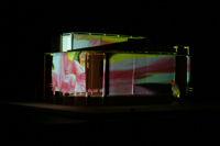 Image of festival parade cast against the side of the CompuObscura, long shot from corner of the device. Taken by Cal Poly Architecture class students using class-created model and slide projector, Spring 2004.