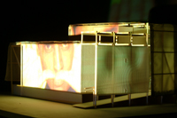 Image of large face from live video footage projected on the side of the CompuObscura model. Taken by Cal Poly Architecture class students using class-created model and slide projector, Spring 2004.